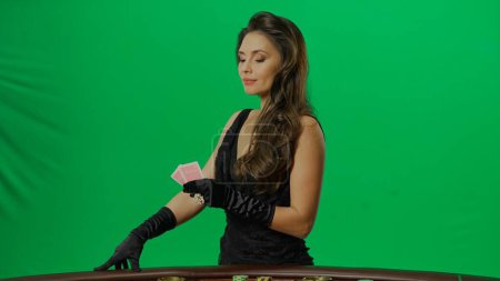 Photo for Casino and gambling commercial advertisement concept. Elegant female in studio on chroma key green screen background. Attractive woman in black dress looking at cards at the camera. - Royalty Free Image