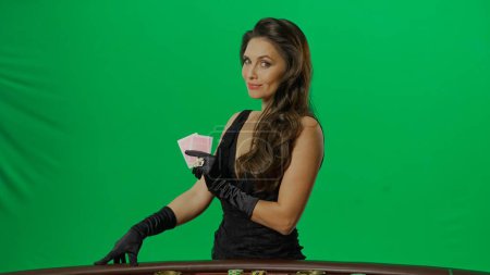 Photo for Casino and gambling commercial advertisement concept. Elegant female in studio on chroma key green screen background. Attractive woman in black dress looking at camera holding few cards. - Royalty Free Image