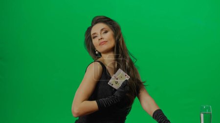 Photo for Casino and gambling commercial advertisement concept. Elegant female in studio on chroma key green screen background. Attractive woman in black dress looking at camera shows ace cards, smiling. - Royalty Free Image