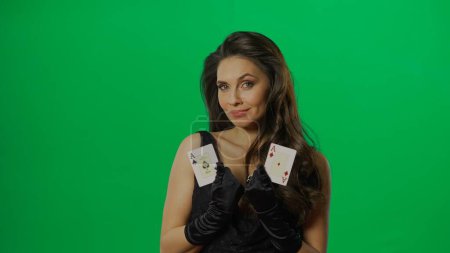 Photo for Casino and gambling commercial advertisement concept. Elegant female in studio on chroma key green screen background. Attractive woman in black dress with pair of ace cards poses at camera. - Royalty Free Image