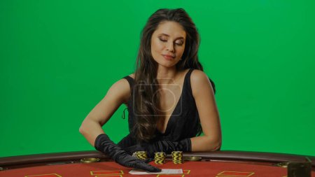 Photo for Casino and gambling commercial advertisement concept. Female in studio on chroma key green screen isolated background. Woman in black dress at the blackjack poker table laying hands on the cards. - Royalty Free Image