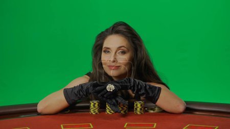 Photo for Casino and gambling commercial advertisement concept. Female in studio on chroma key green screen isolated background. Woman in black dress at the blackjack poker table laying hands on chips. - Royalty Free Image