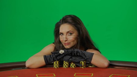 Photo for Casino and gambling commercial advertisement concept. Female in studio on chroma key green screen isolated background. Woman in black dress at the blackjack table smiling laying hands on chips. - Royalty Free Image