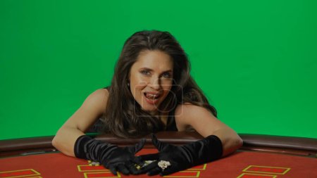 Photo for Casino and gambling commercial advertisement concept. Female in studio on chroma key green screen isolated background. Woman in black dress at the blackjack table smiling takes the winning chips. - Royalty Free Image
