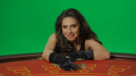 Photo for Casino and gambling commercial advertisement concept. Female in studio on chroma key green screen isolated background. Woman in black dress at the blackjack table smiling holds winning chips. - Royalty Free Image
