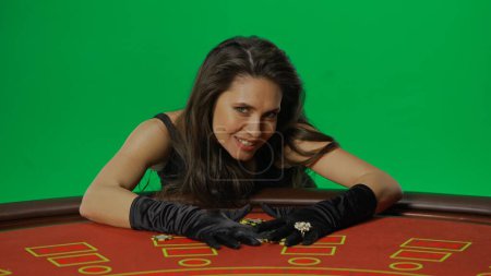 Photo for Casino and gambling commercial advertisement concept. Female in studio on chroma key green screen isolated background. Woman in black dress at the blackjack table smiling holds hands on winning chips. - Royalty Free Image