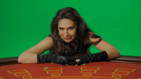 Photo for Casino and gambling commercial advertisement concept. Female in studio on chroma key green screen isolated background. Woman in black dress happy at the blackjack table smiling hands on winning chips. - Royalty Free Image