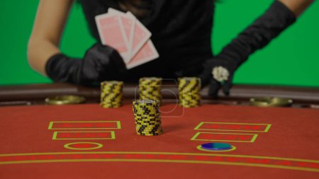 Photo for Casino and gambling commercial advertisement concept. Female in studio on chroma key green screen isolated background. Woman in black dress at the blackjack table focus on stack of chips. - Royalty Free Image