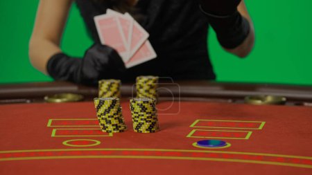 Photo for Casino and gambling commercial advertisement concept. Female in studio on chroma key green screen isolated background. Woman in black dress at the poker table focus on stacks of chips. - Royalty Free Image