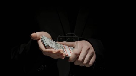 Photo for Business and money creative advertisement concept. Portrait of female in black suit isolated on black background in low light. Woman holding big wad of dollar banknotes. - Royalty Free Image