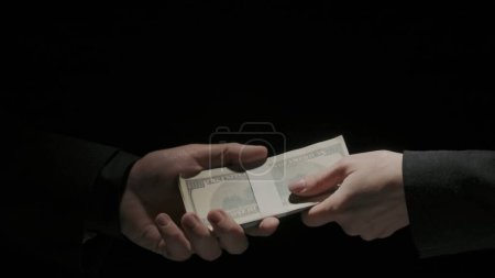 Photo for Business partnership and money corruption creative concept. Portrait of business people in suits on black background. Man gives to woman colleague wad of dollar banknotes making handshake, close up. - Royalty Free Image