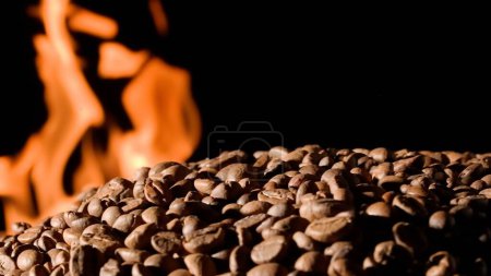 Téléchargez les photos : Les grains de café sur un fond de studio noir avec des langues brûlantes de flamme. Le processus de torréfaction du café pour faire une boisson revigorante. Concept publicitaire pour un café ou un restaurant - en image libre de droit