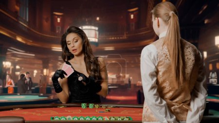 Téléchargez les photos : Femme élégante en robe noire au casino. Belle femme à la table de poker de blackjack. Femme tenant des cartes et pariant avec des jetons. Croupier féminin en attente de pari. Concept de casino et de jeu - en image libre de droit