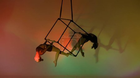 Téléchargez les photos : Chorégraphie moderne et acrobaties concept publicitaire créatif. Portrait d'acrobates femelles isolé fond coloré. Deux filles aerialists danseurs montrent élément dans l'air sur cube avec cordes. - en image libre de droit