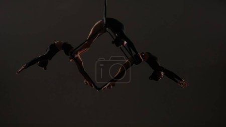 Photo for Modern choreography and acrobatics creative advertisement concept. Portrait of female acrobats isolated black background. Girls aerialists dancers trio holding spinning in the air on cube with ropes. - Royalty Free Image