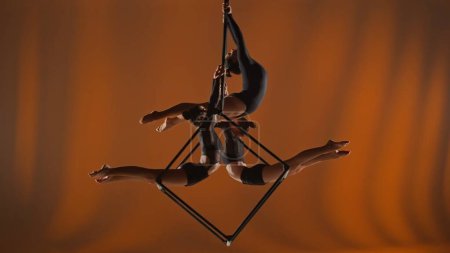 Photo for Modern choreography and acrobatics creative advertisement concept. Portrait of female acrobats isolated on orange background. Girls aerialists dancers trio spinning in the air on cube with ropes. - Royalty Free Image