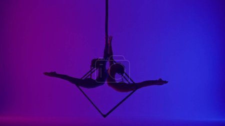 Photo for Modern choreography and acrobatics creative advertisement concept. Silhouette of two female acrobats isolated on neon background. Girls aerialist dancers spinning in splits in air on cube with ropes. - Royalty Free Image