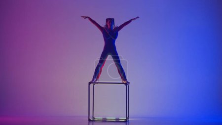 Photo for Modern choreography and acrobatics creative advertisement concept. Silhouette of two female acrobats isolated on neon vivid background. Girls gymnastic dancers performing acrobatic element on cube. - Royalty Free Image