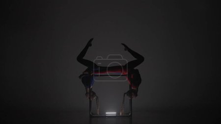 Téléchargez les photos : Chorégraphie moderne et acrobaties concept publicitaire créatif. Portrait de deux acrobates femelles isolées sur fond noir. Filles danseuses aériennes en costume bleu rouge démontrant pose à l'intérieur du cube. - en image libre de droit