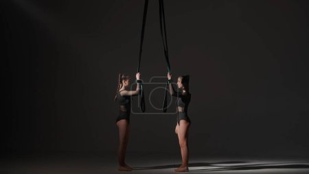 Téléchargez les photos : Chorégraphie moderne et acrobaties concept publicitaire créatif. Portrait de deux acrobates en studio isolées sur fond noir. Filles danseurs aériens élément performant avec des cordes. - en image libre de droit