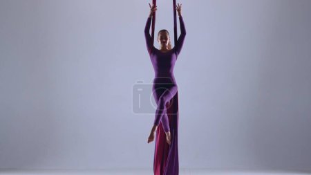 Photo for Modern choreography and acrobatics creative advertisement concept. Female artist isolated on blue neon studio background. Girl aerial dancer performing floating element on air silk. - Royalty Free Image