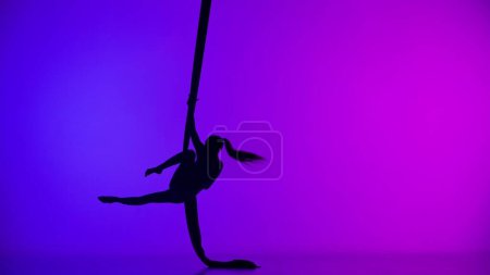 Téléchargez les photos : Chorégraphie moderne et acrobaties concept publicitaire créatif. Silhouette d'acrobate femelle isolée sur fond néon coloré. Danseuse aérienne exécutant un élément acrobatique sur soie aérienne. - en image libre de droit