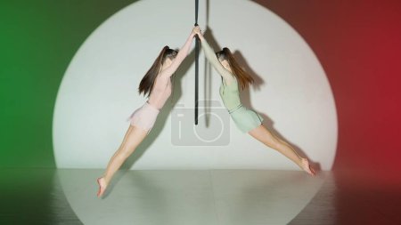 Téléchargez les photos : Chorégraphie moderne et acrobaties concept publicitaire créatif. Deux gymnastes isolées sur fond de studio rouge-vert. Filles danseuses aériennes montrant élément acrobatique sur anneau avec sangles. - en image libre de droit