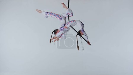Téléchargez les photos : Chorégraphie moderne et acrobaties concept publicitaire créatif. Deux gymnastes isolées sur fond de studio blanc. Filles danseuses aériennes en tenues étincelantes filant sur anneau. - en image libre de droit