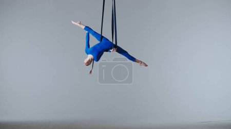 Photo for Modern choreography and acrobatics creative advertisement concept. Female gymnast isolated on white studio background. Girl aerial dancer balancing spinning on gymnastic straps, showing dance elements - Royalty Free Image