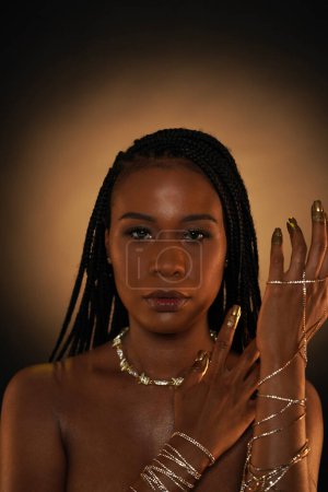 Foto de Retrato de una joven afroamericana con joyas de oro. Los modelos de brazos están entrelazados con cadenas de oro, y hay un collar alrededor de su cuello. El oro líquido se aplica a los dedos y las uñas - Imagen libre de derechos