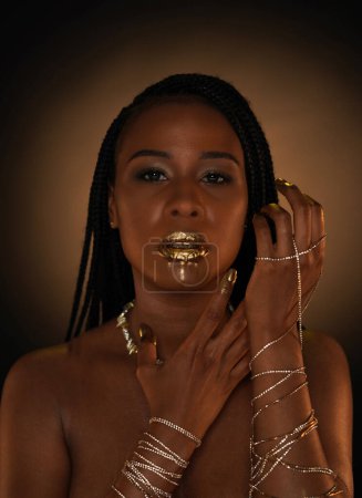 Téléchargez les photos : Portrait d'une jeune afro-américaine avec des chaînes en or sur les mains et un collier sur le cou. L'or liquide est appliqué sur les lèvres des modèles et s'écoule dans les ruisseaux minces. Concept beauté. Gros plan - en image libre de droit