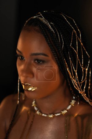 Foto de Retrato de una mujer afroamericana con un collar de oro y cadenas de oro en el pelo. Los modelos de labios y clavículas están cubiertos de oro líquido. De cerca. El concepto de belleza - Imagen libre de derechos