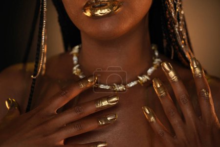 Téléchargez les photos : Portrait d'une femme afro-américaine avec un collier en or autour du cou. Les modèles lèvres, doigts et ongles sont recouverts d'or liquide. Ferme là. Le concept de beauté - en image libre de droit