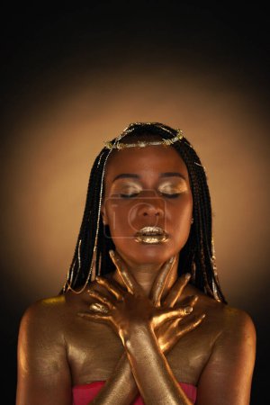 Foto de Retrato de una mujer afroamericana con joyas de oro en el pelo. Los modelos brazos, cuello y hombros están cubiertos de oro líquido. Primer plano. El concepto de belleza - Imagen libre de derechos