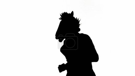 Téléchargez les photos : Silhouette noire de l'homme en costume d'affaires avec masque de tête de cheval sur fond de studio isolé blanc. L'homme d'affaires court vite. Concept de travail de bureau dur - en image libre de droit