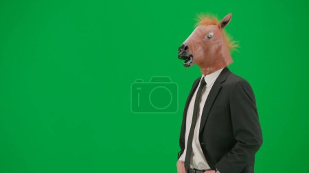 Téléchargez les photos : Homme en costume d'affaires avec masque de tête de cheval sur fond de studio vert. Homme d'affaires. Concept de travail de bureau dur Demi tour - en image libre de droit