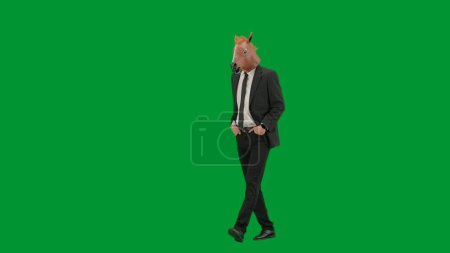 Téléchargez les photos : Homme en costume d'affaires avec masque de tête de cheval sur fond de studio vert. Homme d'affaires marchant et gardant les mains dans les poches du pantalon. Concept de travail de bureau dur Demi tour - en image libre de droit