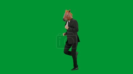 Téléchargez les photos : Homme en costume d'affaires avec masque de tête de cheval sur fond de studio vert. Homme d'affaires marchant, rebondissant et dansant. Concept de travail de bureau dur Demi tour - en image libre de droit