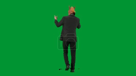 Photo for Man in business suit with horse head mask on green studio background. Businessman walking and talking on smartphone. Concept of hard office work Back view - Royalty Free Image