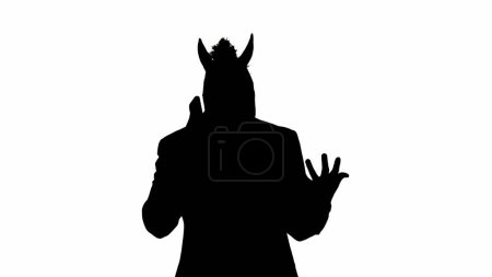 Téléchargez les photos : Silhouette noire d'homme en costume d'affaires avec masque de tête de cheval sur fond de studio blanc. Un homme d'affaires parle sur un smartphone, se met en colère et crie dans le téléphone. Concept de travail de bureau dur - en image libre de droit