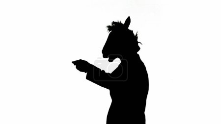 Téléchargez les photos : Silhouette noire de l'homme en costume d'affaires avec masque de tête de cheval sur fond de studio isolé blanc. Homme d'affaires dansant joyeusement. Concept de travail de bureau dur - en image libre de droit
