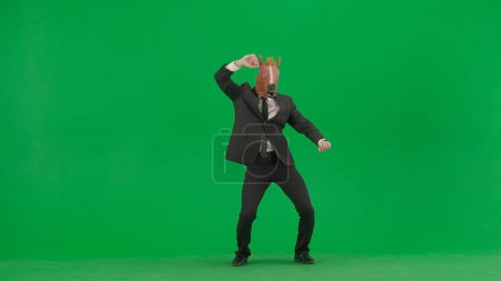 Téléchargez les photos : Un homme en costume d'affaires avec un masque de tête de cheval sur fond de studio vert. Homme d'affaires dansant joyeusement. Concept de travail de bureau dur - en image libre de droit