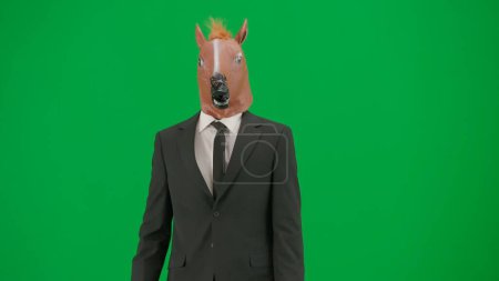 Téléchargez les photos : Homme en costume d'affaires avec masque de tête de cheval sur fond de studio vert. Homme d'affaires. Concept de travail de bureau dur - en image libre de droit