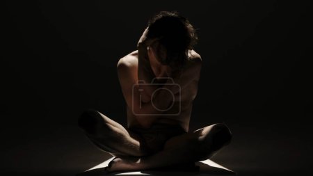 Photo for Body beauty and healthcare creative advertisement concept, Portrait of male model in studio on the black background under spotlight. Attractive man silhouette sitting touching himself at the camera. - Royalty Free Image