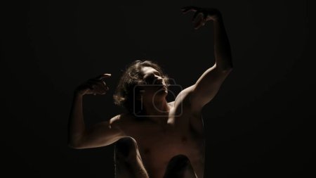 Photo for Body beauty and healthcare creative advertisement concept, Portrait of male model in studio on the black background under spotlight. Attractive man silhouette posing hands up at the camera. - Royalty Free Image