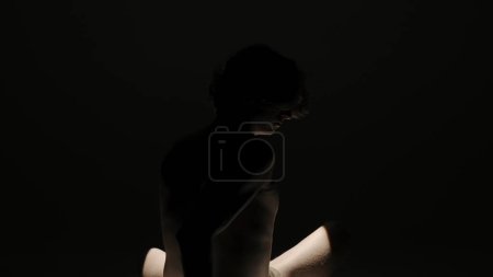 Foto de Body beauty and healthcare creative advertisement concept, Retrato de modelo masculino en estudio sobre fondo negro bajo el foco. Atractiva silueta de hombre girando a la cámara. - Imagen libre de derechos