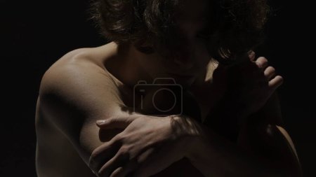 Photo for Body beauty and healthcare creative advertisement concept, Portrait of male model in studio on the black background under spotlight. Attractive man silhouette holding shoulder at the camera. - Royalty Free Image