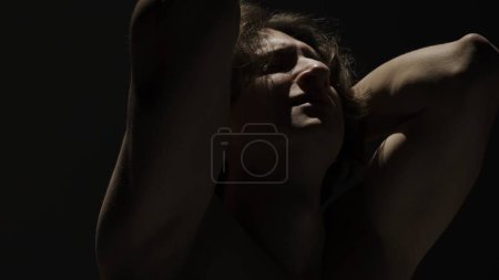 Photo for Body beauty and healthcare creative advertisement concept, Portrait of male model in studio on the black background under spotlight. Attractive man silhouette emotional face expression at the camera. - Royalty Free Image