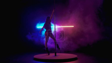 Photo for Woman in yellow reflective underwear dancing on pole. A dancer performs tricks on a pole in a dark studio in the light of red blue neon lights. - Royalty Free Image