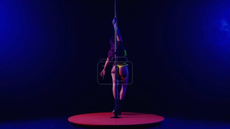 Photo for Elegant pole dance performed by sexy and attractive woman. Woman in yellow lingerie and high heeled shoes dancing on pylon in dark smoky studio, illuminated by spotlight and pink neon light - Royalty Free Image